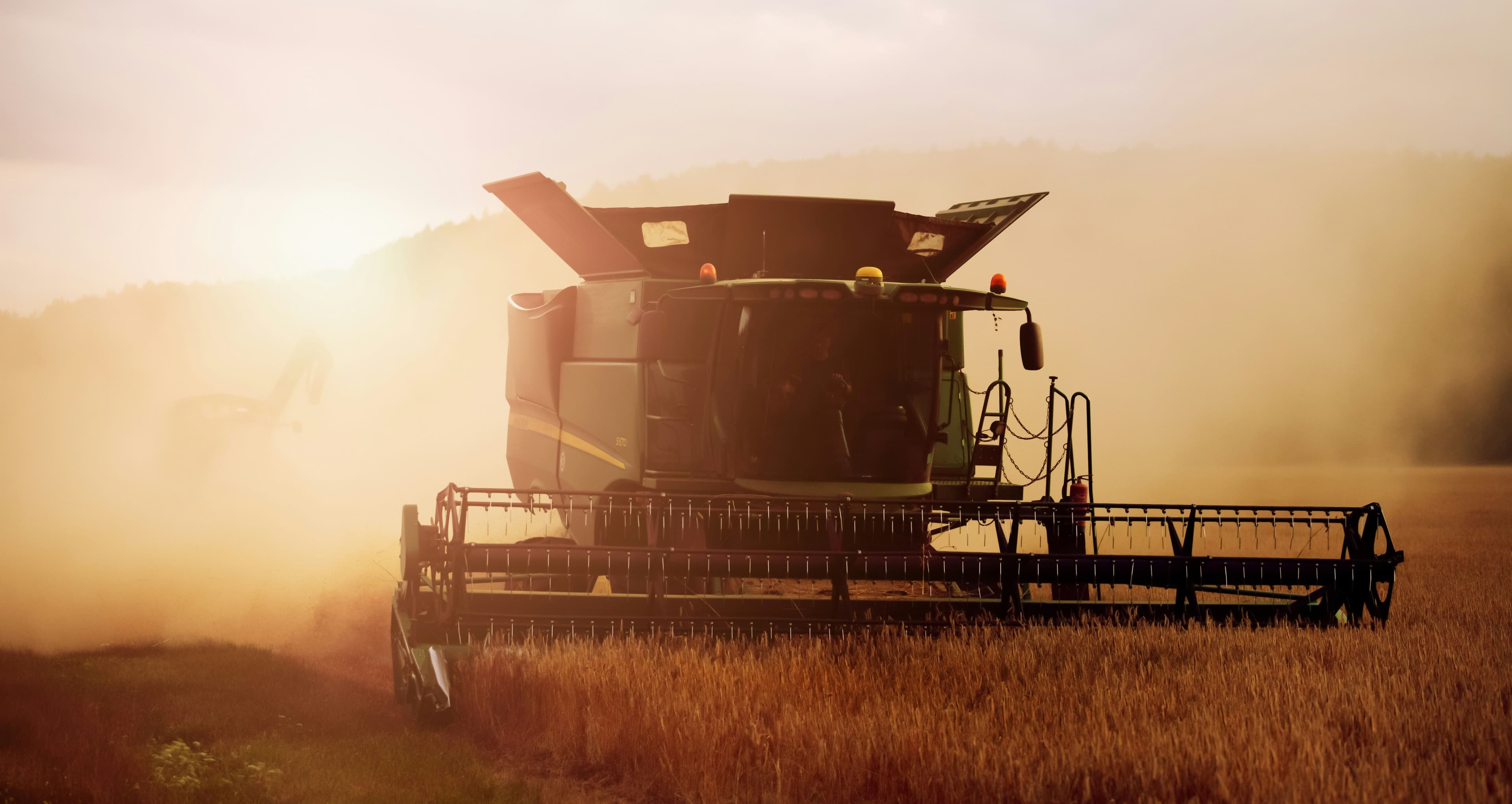 A combine harvester gathering crops in a sunlit field